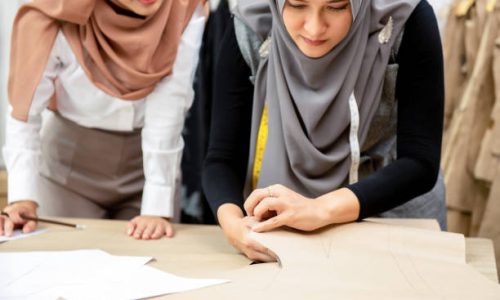 Muslim woman fashion designer working together with her colleague cutting clothing pattern in tailor shop